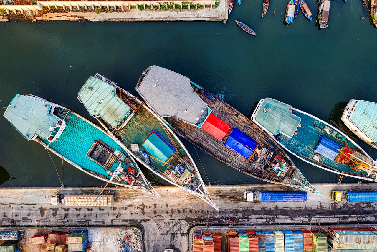 Bird's eye view of colorful boats docked at a marina, showcasing vibrant hues and industrial activity.
